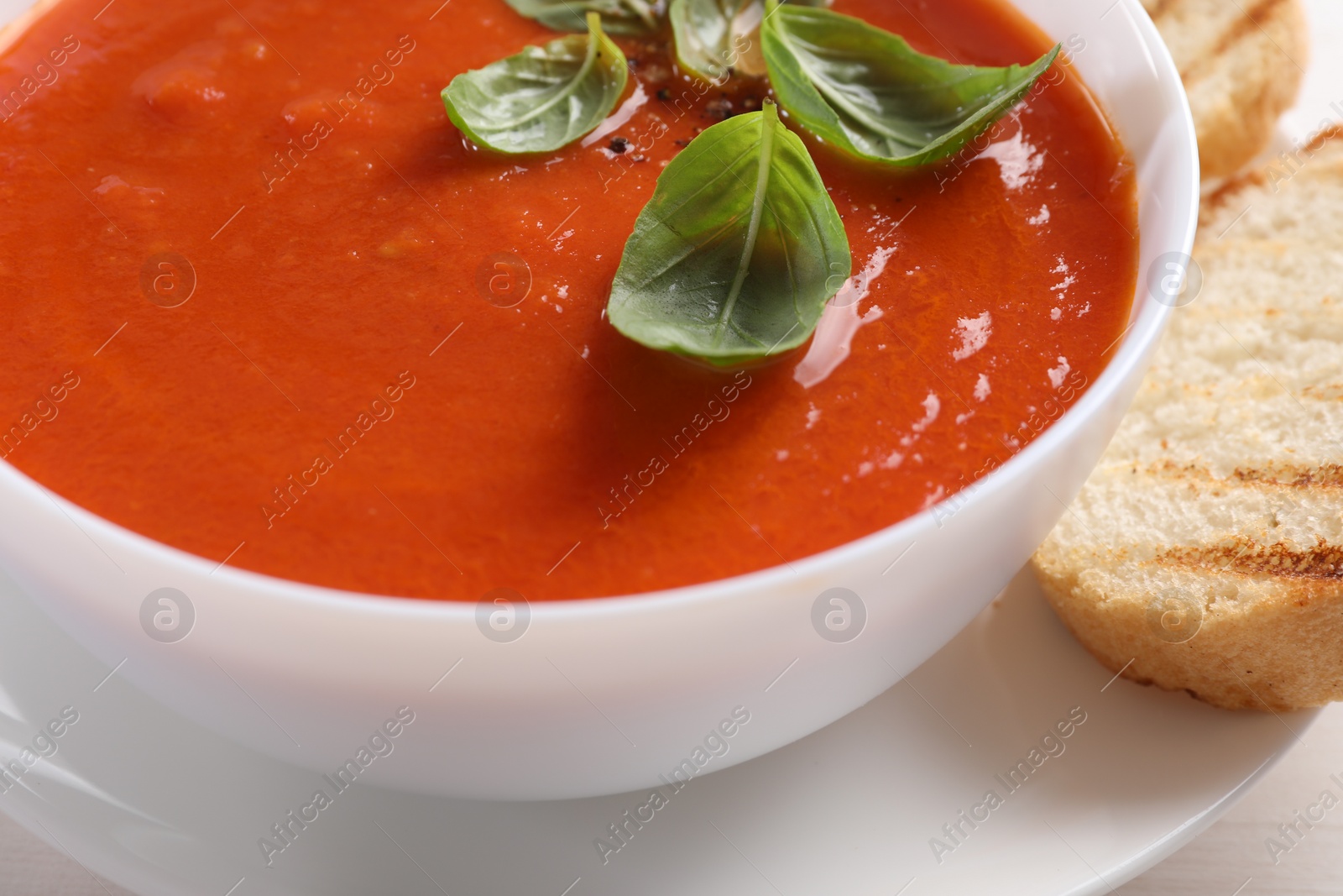 Photo of Delicious tomato cream soup in bowl with pieces of grilled bread on table, closeup