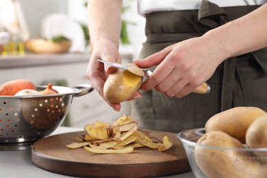 Photo of Woman peeling fresh potato with knife at light table indoors, closeup