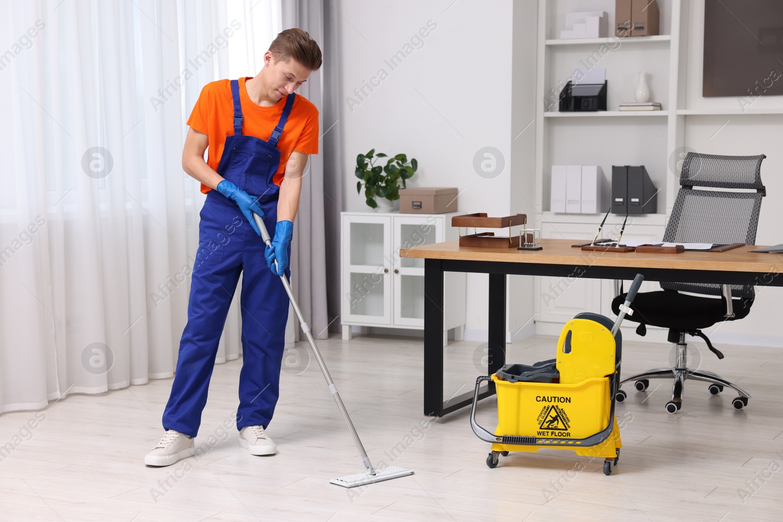 Photo of Cleaning service. Man washing floor with mop in office