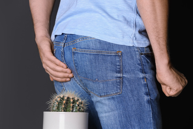 Photo of Man sitting down on cactus against black background, closeup. Hemorrhoid concept