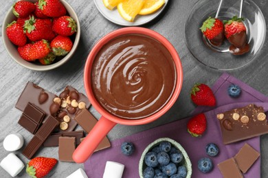 Photo of Fondue pot with melted chocolate, marshmallows, fresh orange and different berries on grey table, flat lay