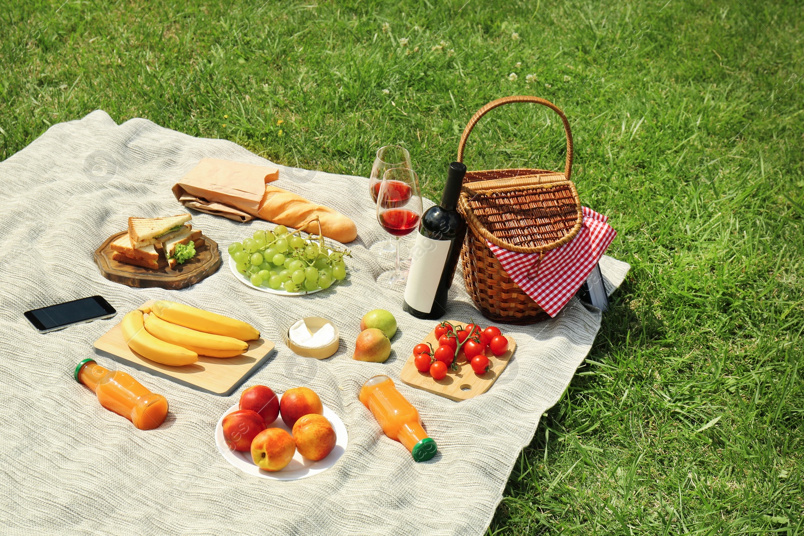 Photo of Wicker basket and food on blanket in park. Summer picnic