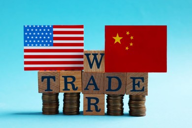 USA and China flags, coins and phrase Trade war made of wooden cubes on light blue background
