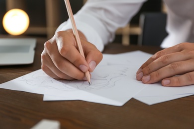 Photo of Man drawing portrait with pencil on sheet of paper at wooden table, closeup