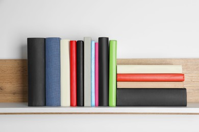 Photo of Different books on wooden shelf near white wall
