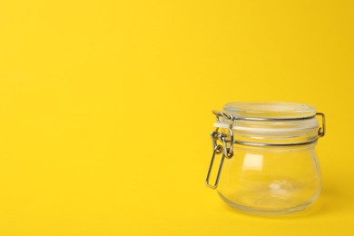 Photo of Closed empty glass jar on yellow background, space for text