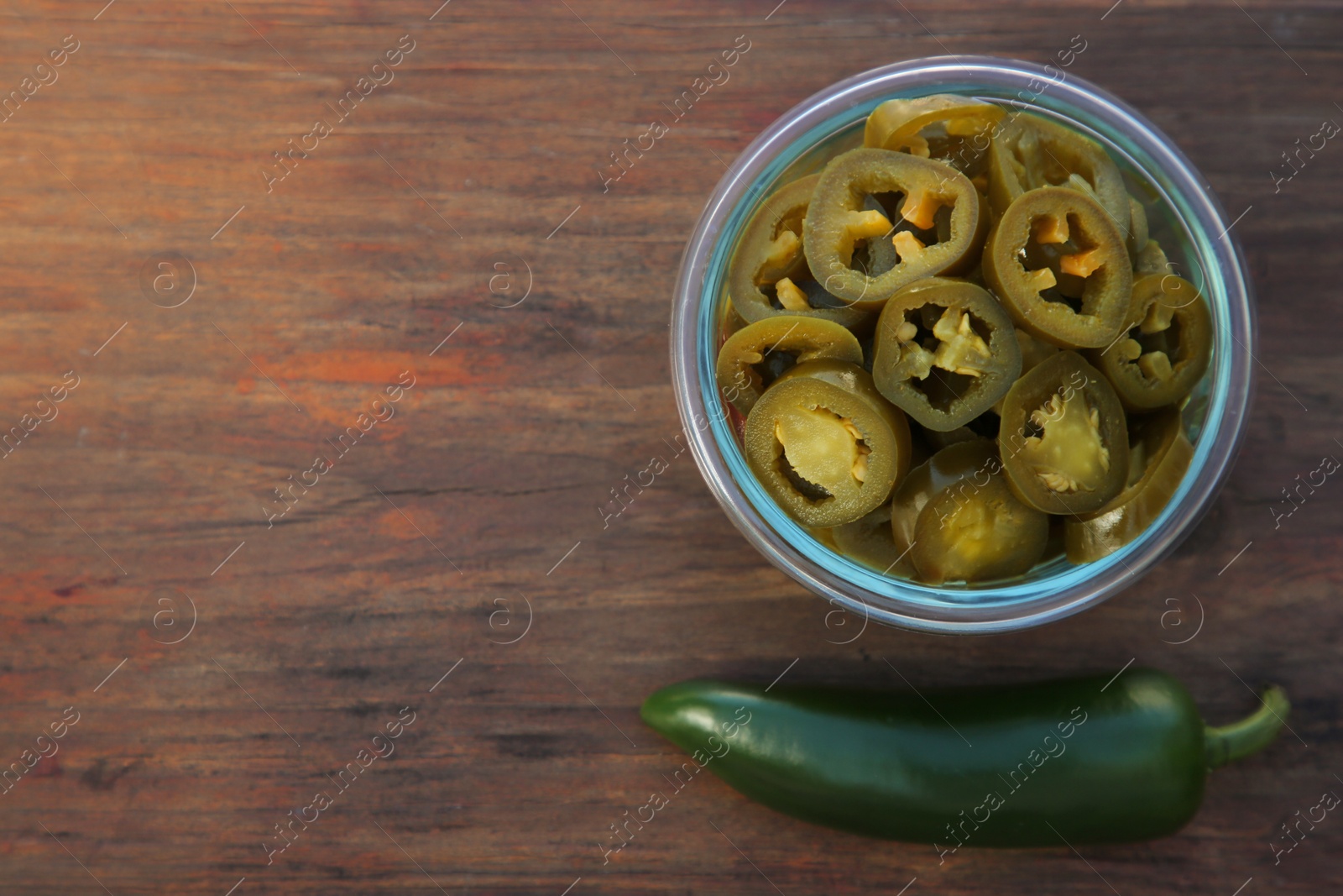 Photo of Fresh and pickled green jalapeno peppers on wooden table, flat lay. Space for text