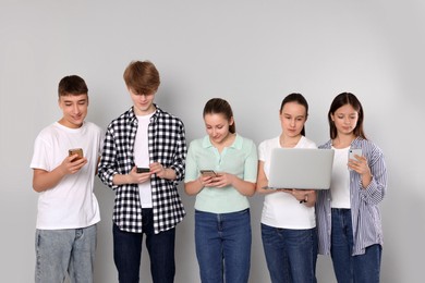 Group of happy teenagers using different gadgets on light grey background