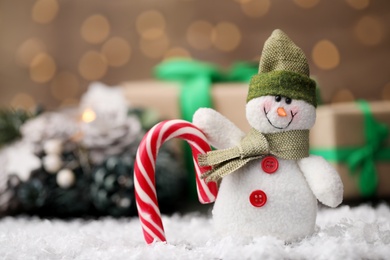 Snowman toy and candy on table against blurred festive lights. Christmas decoration