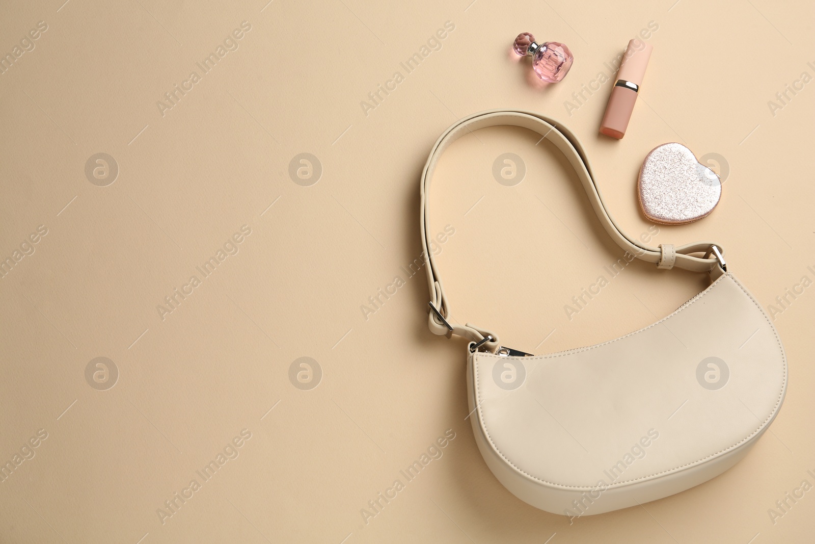 Photo of Stylish baguette bag, perfume, lipstick and pocket mirror on beige background, flat lay, Space for text