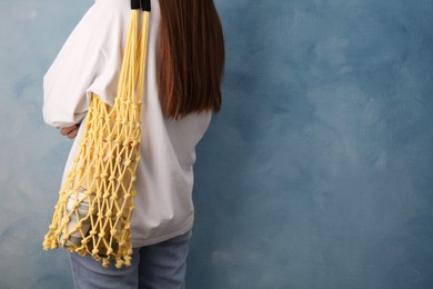 Photo of Woman with net bag full of different items near light blue wall, closeup and space for text. Conscious consumption