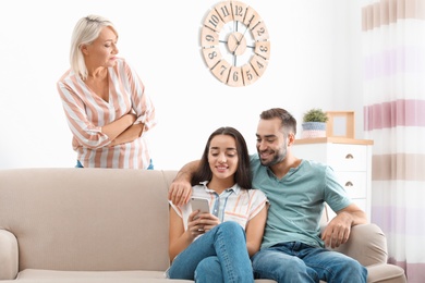 Young couple spending time together in presence of mother-in-law at home