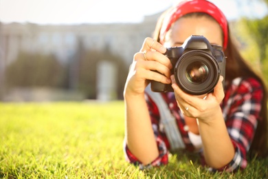 Photo of Young photographer taking picture with professional camera on green grass. Space for text