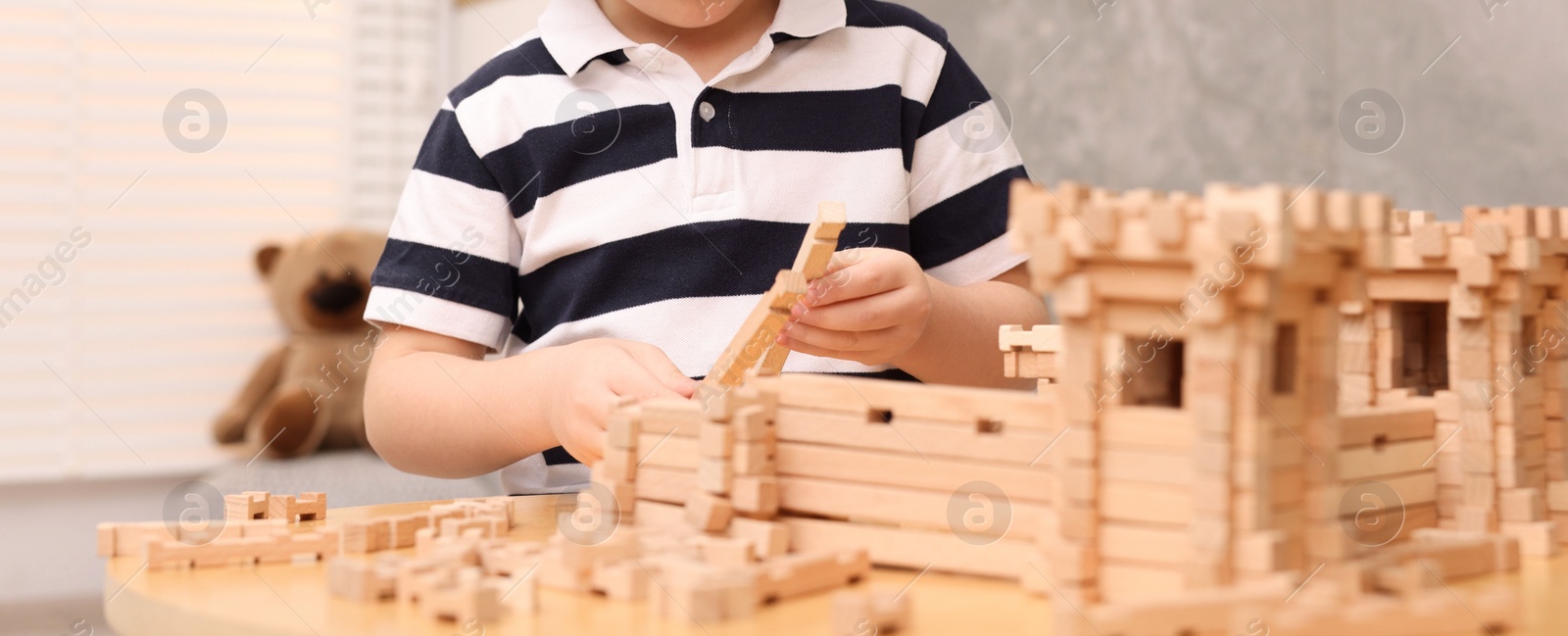 Photo of Little boy playing with wooden construction set at table in room, closeup. Child's toy