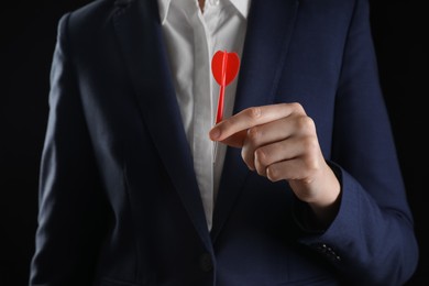 Businesswoman holding red dart on black background, closeup