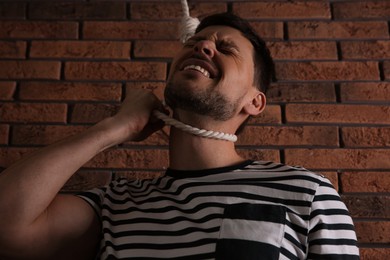 Photo of Depressed man with rope noose on neck near brick wall, low angle view