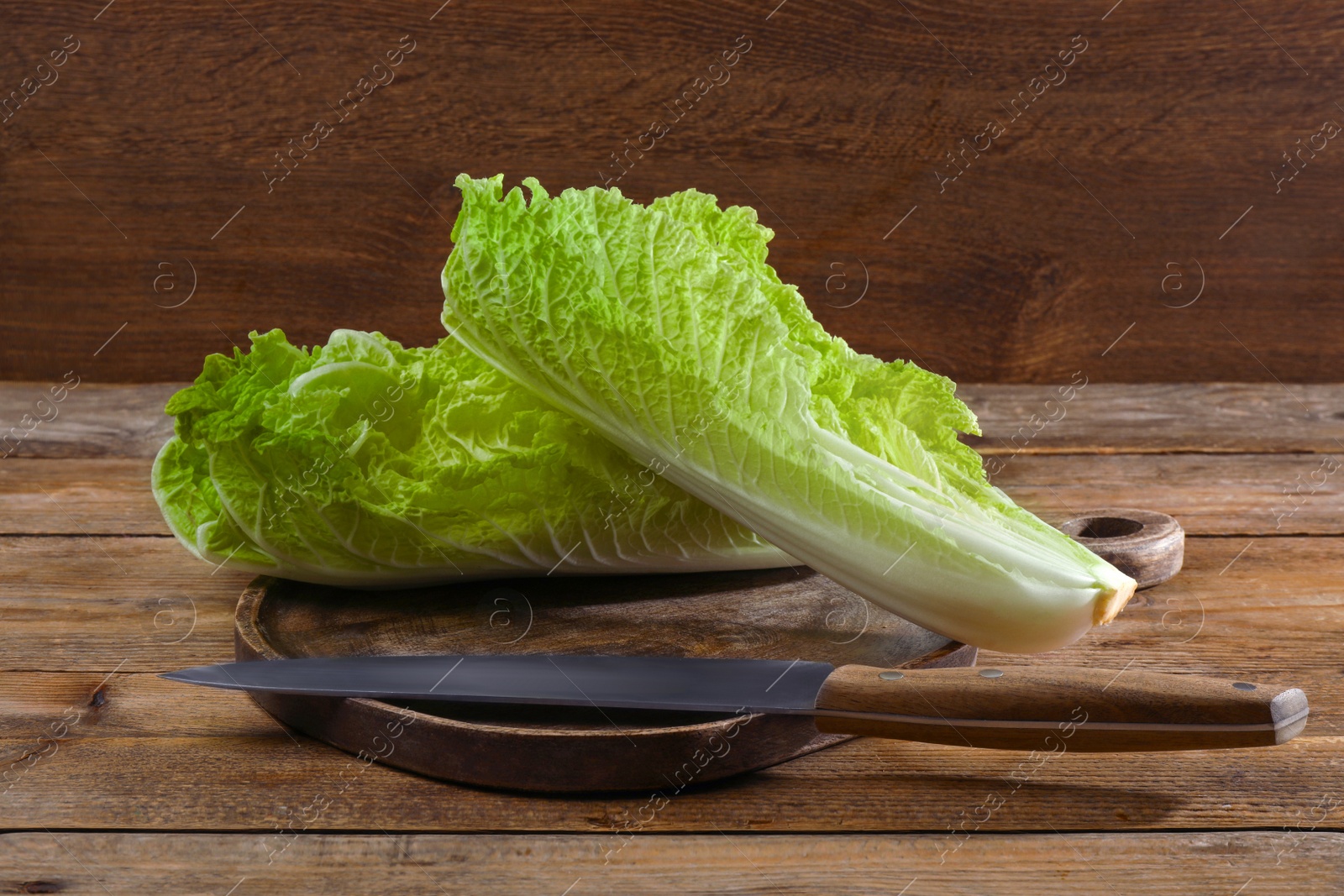 Photo of Halves of fresh ripe Chinese cabbage and knife on wooden table
