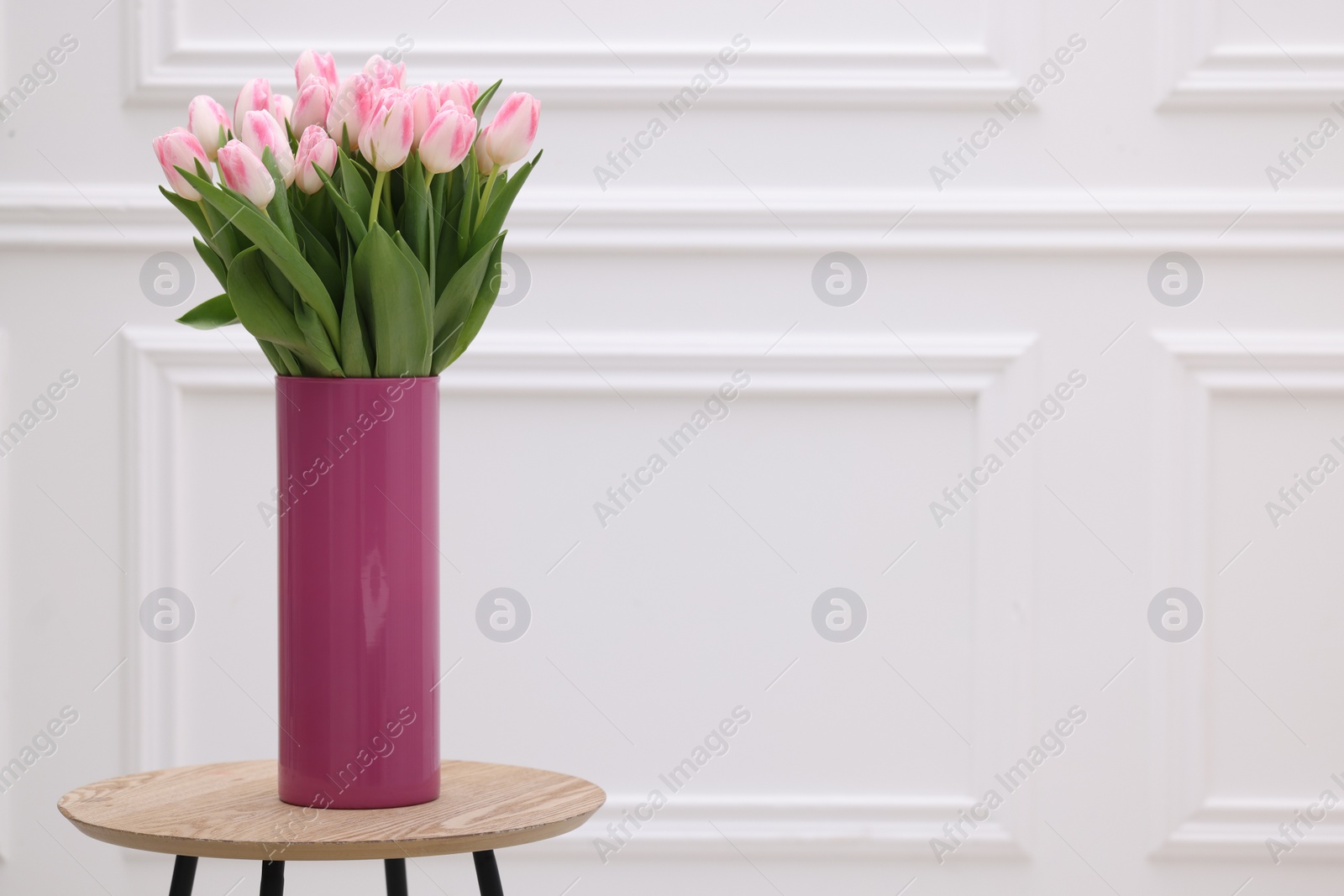 Photo of Beautiful bouquet of fresh pink tulips on table near white wall. Space for text