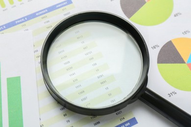 Magnifying glass on accounting documents with data and graphs, closeup