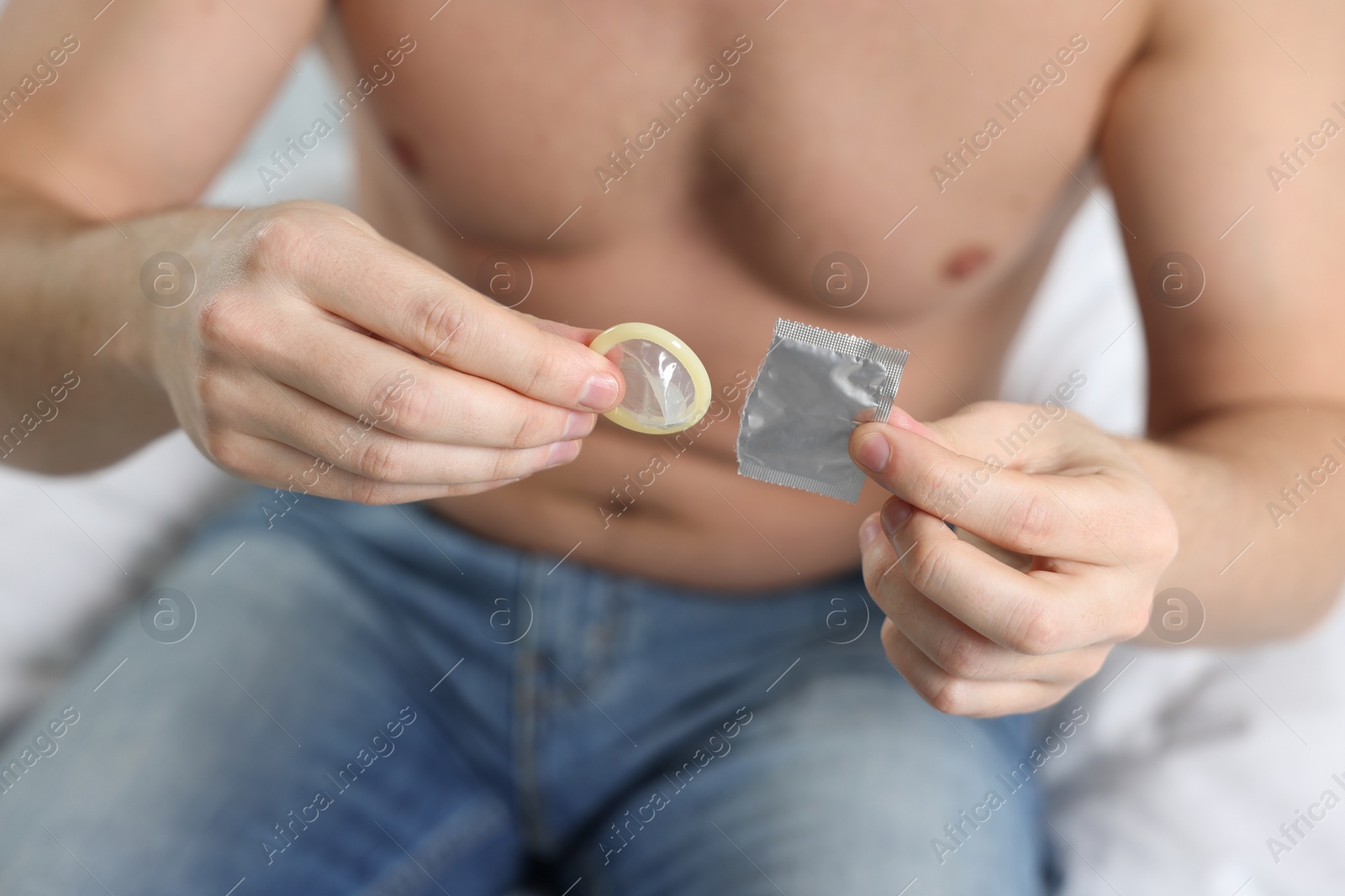 Photo of Closeup of man holding open pack and condom on bed