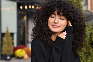 Happy young woman in stylish black sweater outdoors, space for text