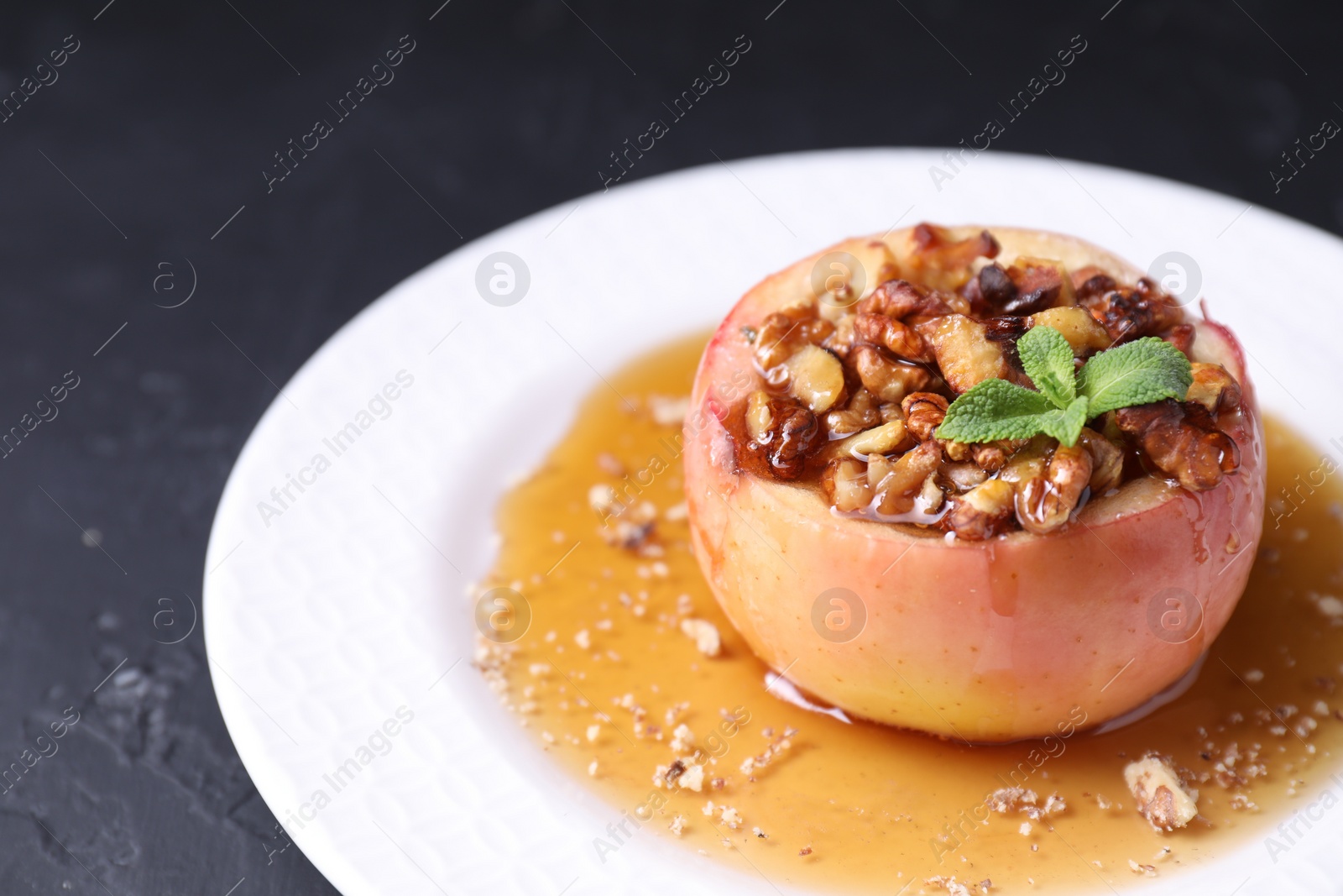 Photo of Tasty baked apple with nuts, honey and mint on gray table, closeup