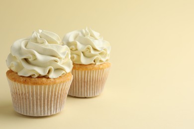 Tasty vanilla cupcakes with cream on pale yellow background, space for text