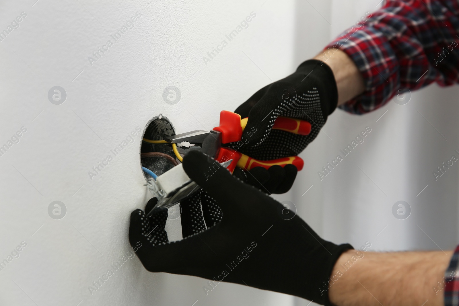 Photo of Electrician with pliers repairing power socket, closeup