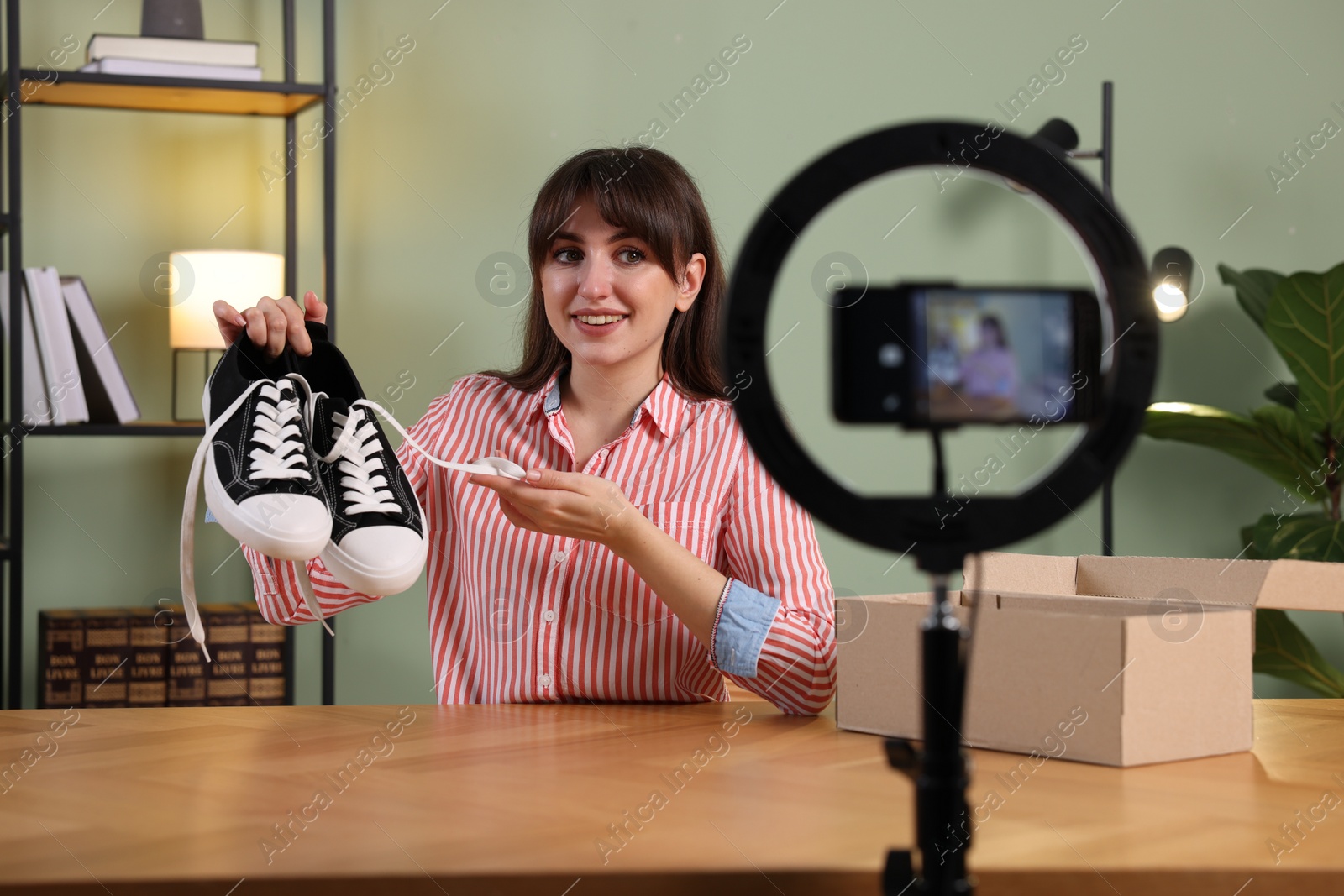 Photo of Smiling fashion blogger recording video while talking about sneakers at home