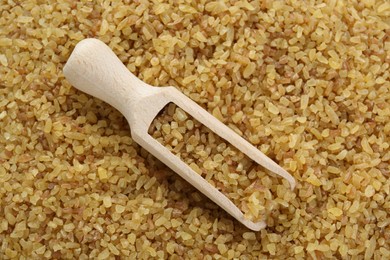 Wooden scoop with cereal on uncooked bulgur, top view