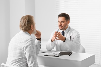 Photo of Doctor consulting senior patient at white table in clinic