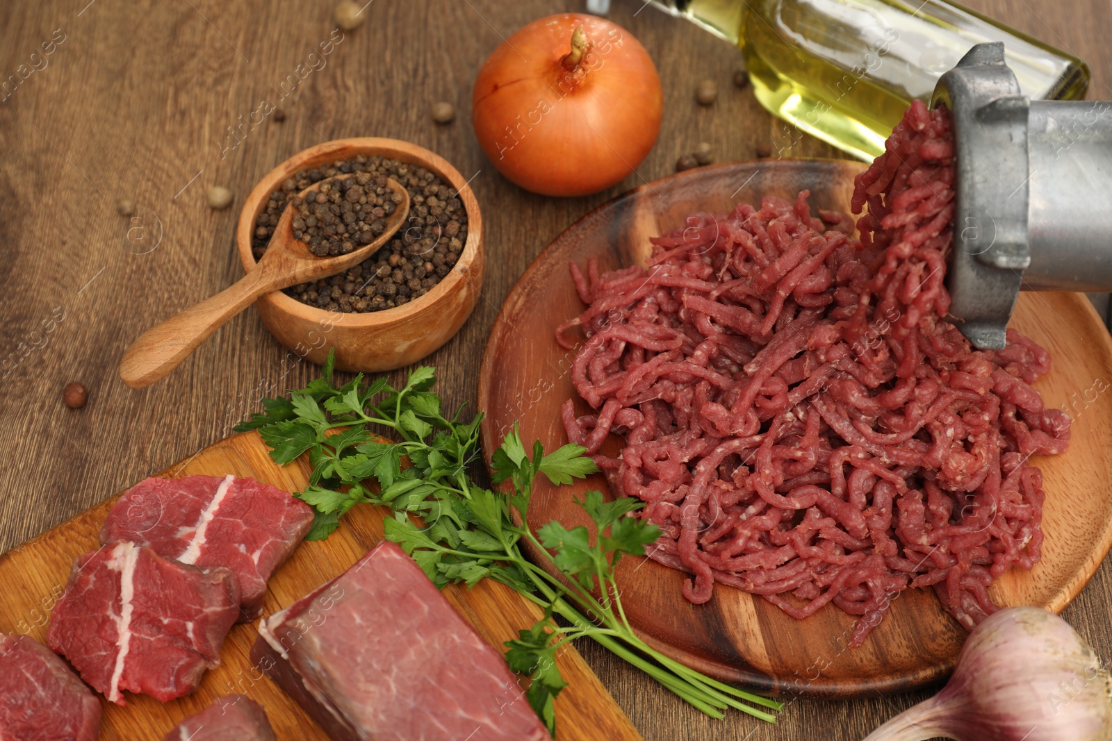 Photo of Meat grinder with beef, garlic, onion, parsley, oil and peppercorns on wooden table