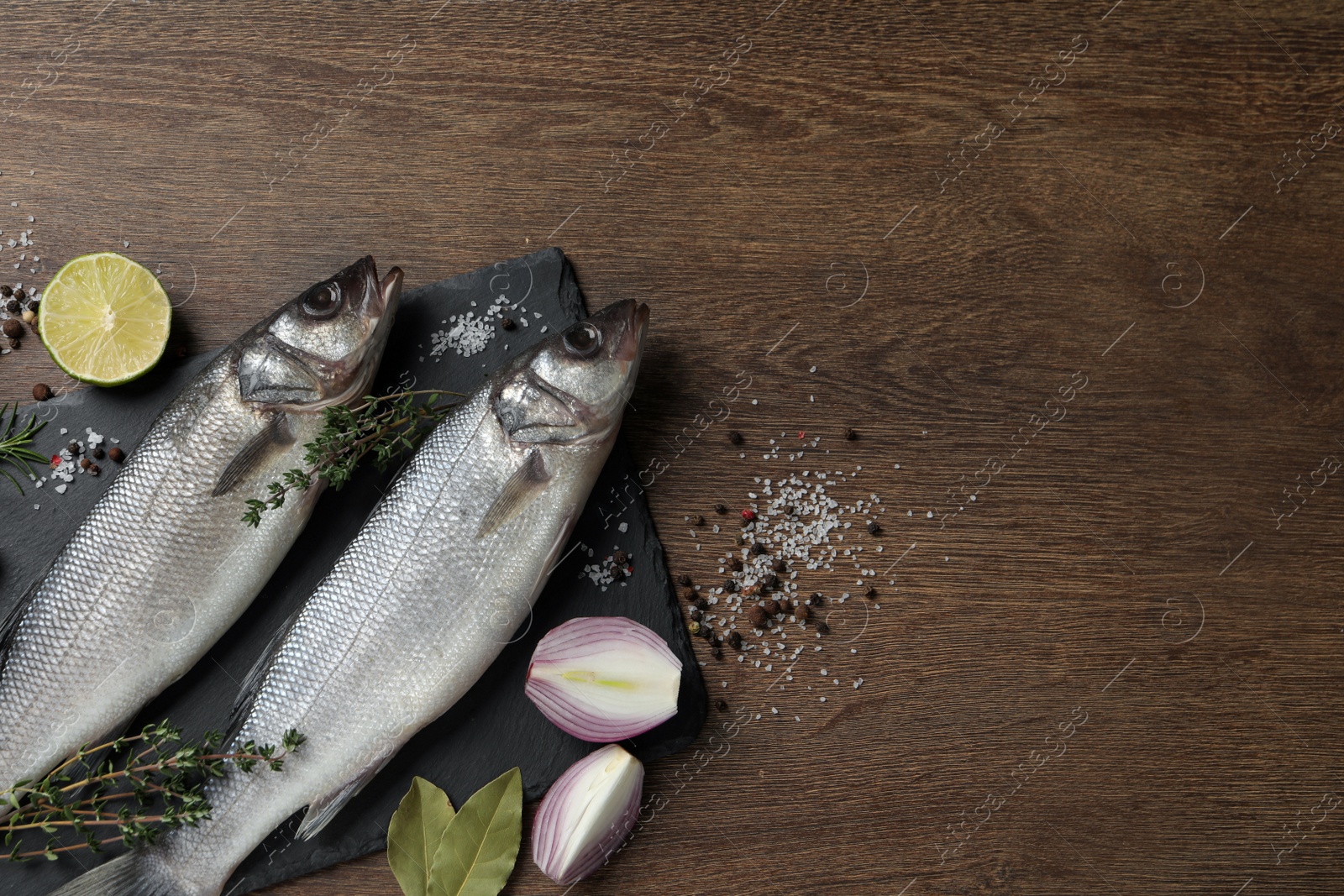 Photo of Sea bass fish and ingredients on wooden table, flat lay. Space for text