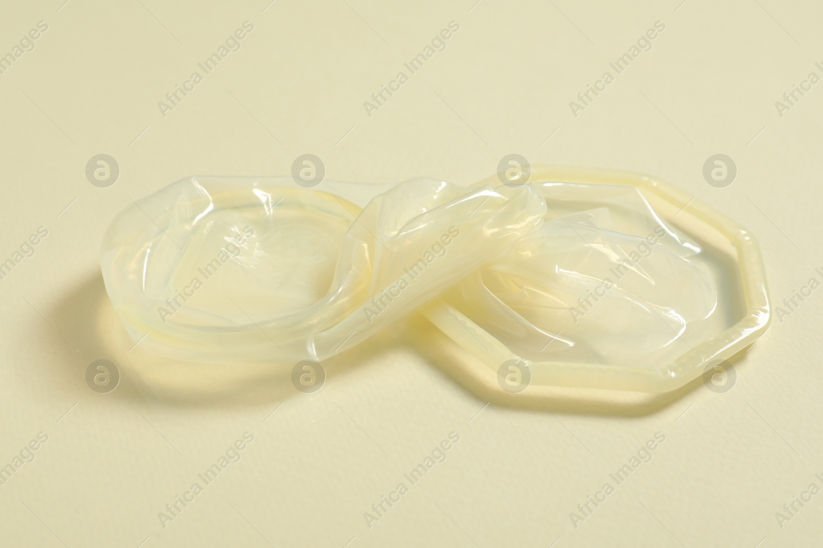 Photo of Unrolled female condom on beige background, closeup. Safe sex