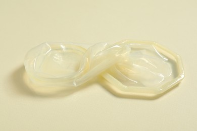 Photo of Unrolled female condom on beige background, closeup. Safe sex