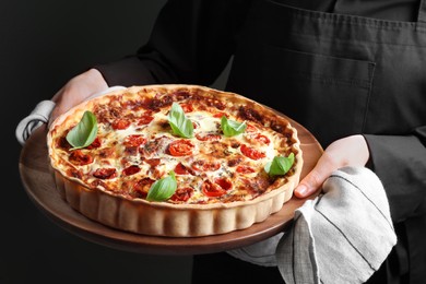 Woman holding delicious homemade quiche with prosciutto on dark background, closeup