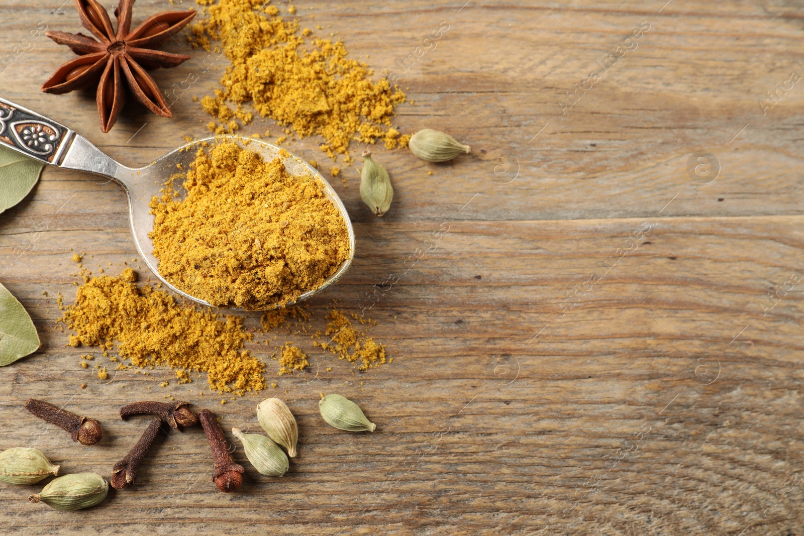 Photo of Spoon with dry curry powder and other spices on wooden table, flat lay. Space for text