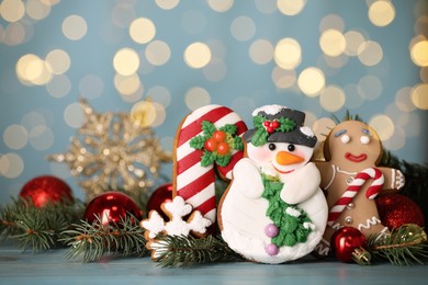 Photo of Sweet Christmas cookies and decor on light blue table against blurred festive lights