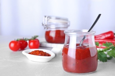 Photo of Jar of hot chili sauce with spoon and ingredients on table. Space for text