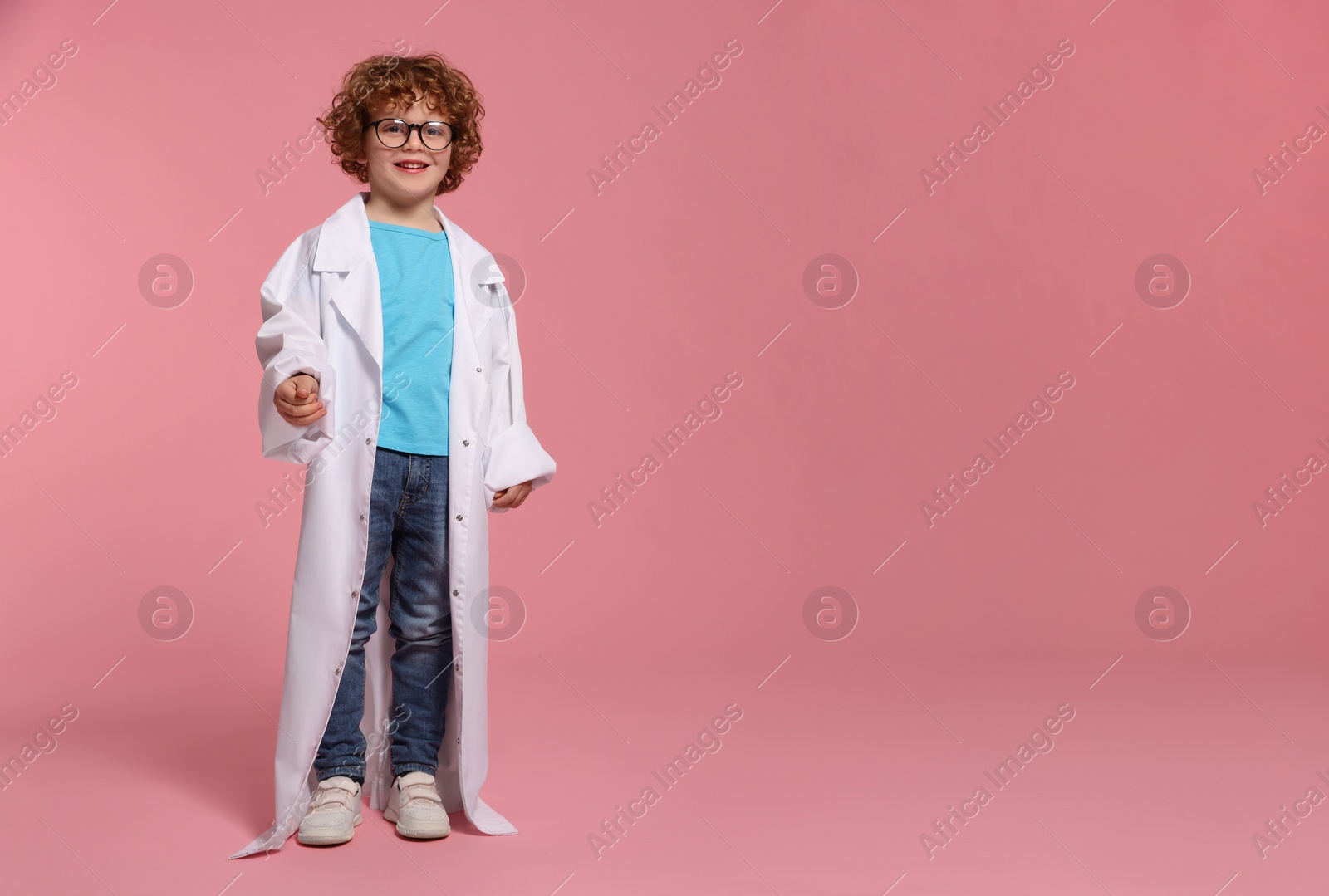 Photo of Full length portrait of little boy in medical uniform and glasses on pink background. Space for text