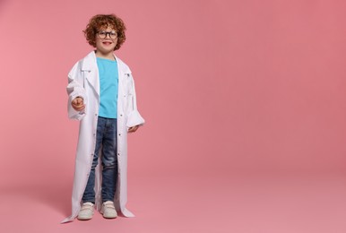 Full length portrait of little boy in medical uniform and glasses on pink background. Space for text