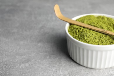 Green matcha powder and bamboo scoop on light grey table, closeup. Space for text