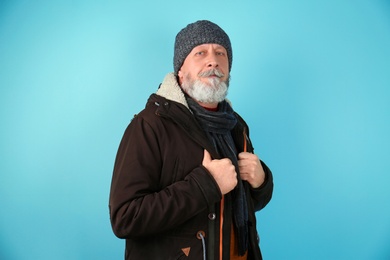 Mature man in warm clothing on color background. Ready for winter vacation