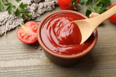 Photo of Bowl and spoon with tasty ketchup, fresh tomatoes, parsley and spices on wooden table