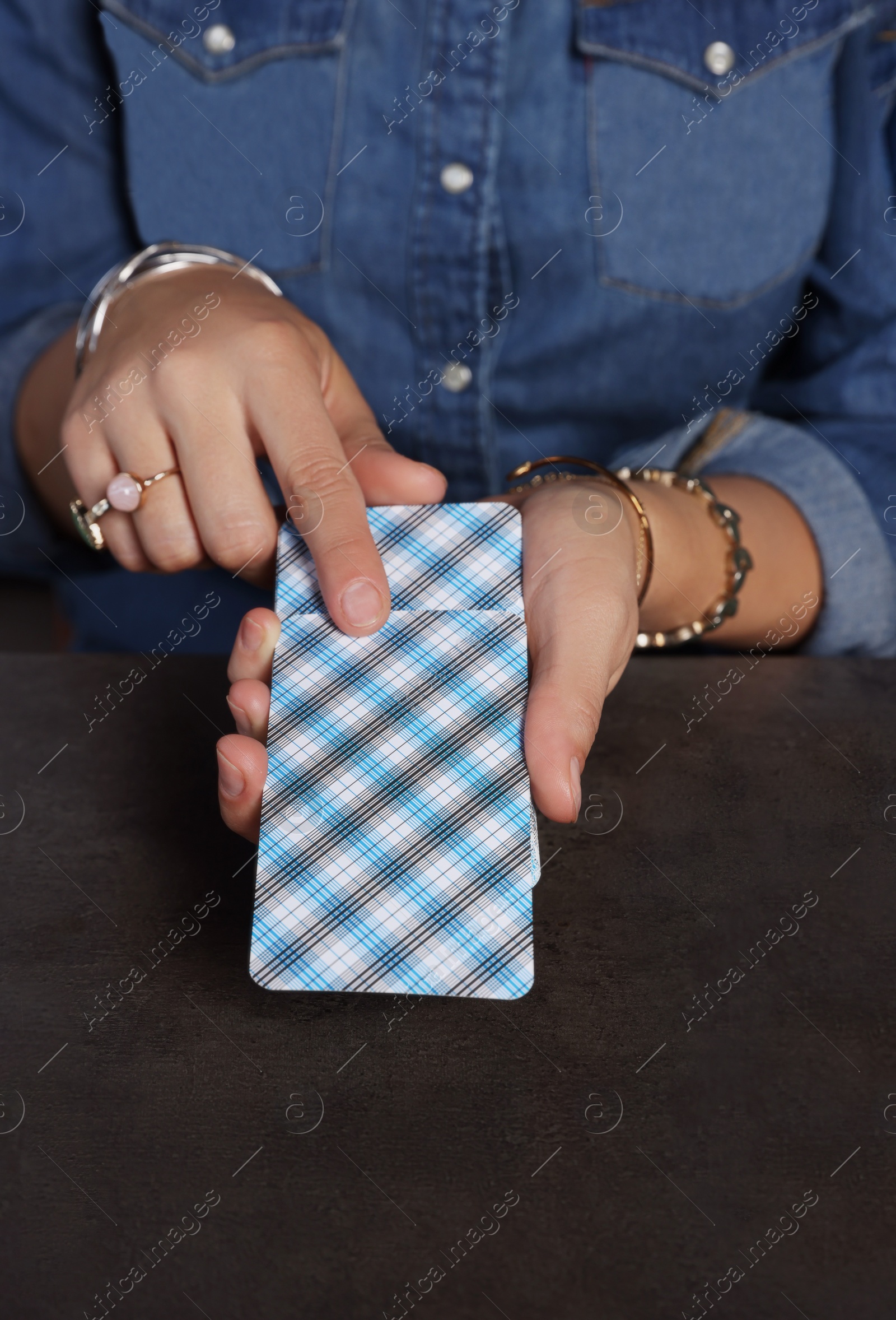 Photo of Fortune teller with deck of tarot cards at grey table, closeup