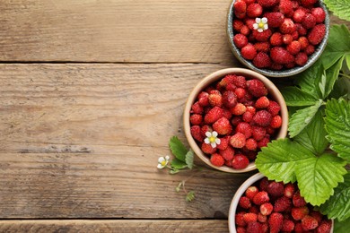 Photo of Fresh wild strawberries in bowls and leaves on wooden table, flat lay. Space for text