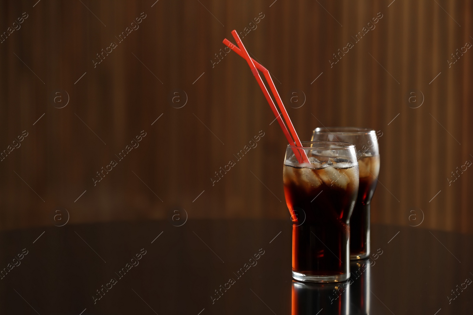 Photo of Glasses of cola with ice on table against blurred background. Space for text