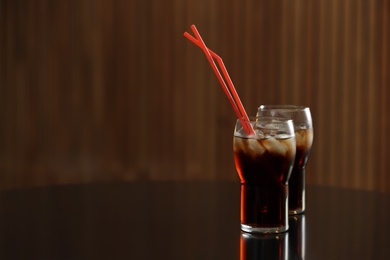 Glasses of cola with ice on table against blurred background. Space for text