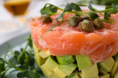 Photo of Tasty salmon tartare with avocado, capers and microgreens on plate, closeup