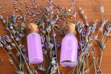 Photo of Beautiful lavender flowers and bottles with essence oil on wooden table, closeup